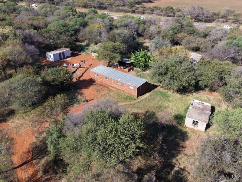 Aerial view of a rural farm property featuring multiple detached brick structures with corrugated metal roofs set within a natural, wooded landscape.