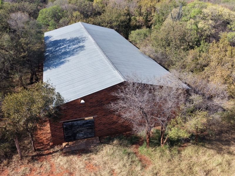Aerial view of a face brick farm building featuring a corrugated metal roof and a metal roller door, situated in a wooded area.