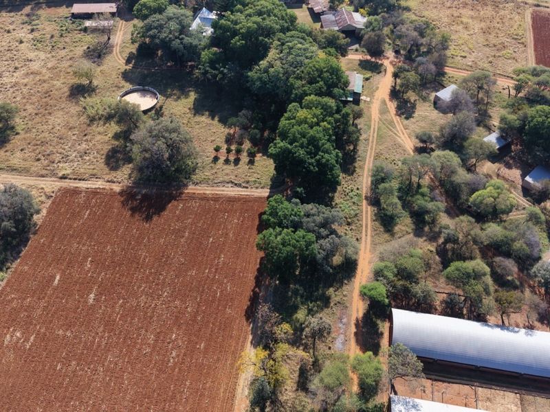 Aerial view of a farm property featuring cultivated fields, multiple outbuildings, a circular livestock pen, and established tree lines.