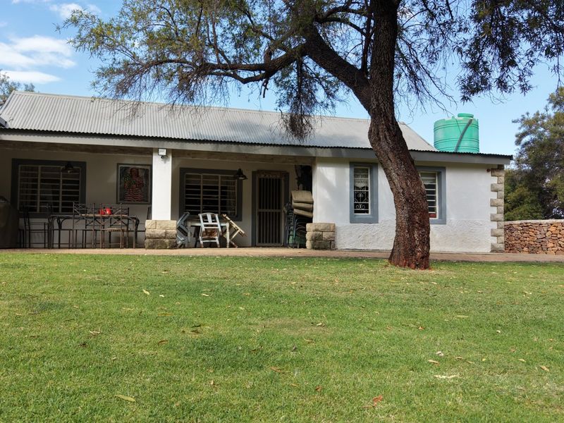 Rear view of a farm-style dwelling featuring a covered patio, corrugated metal roofing, stone accents, and an adjacent water storage tank.