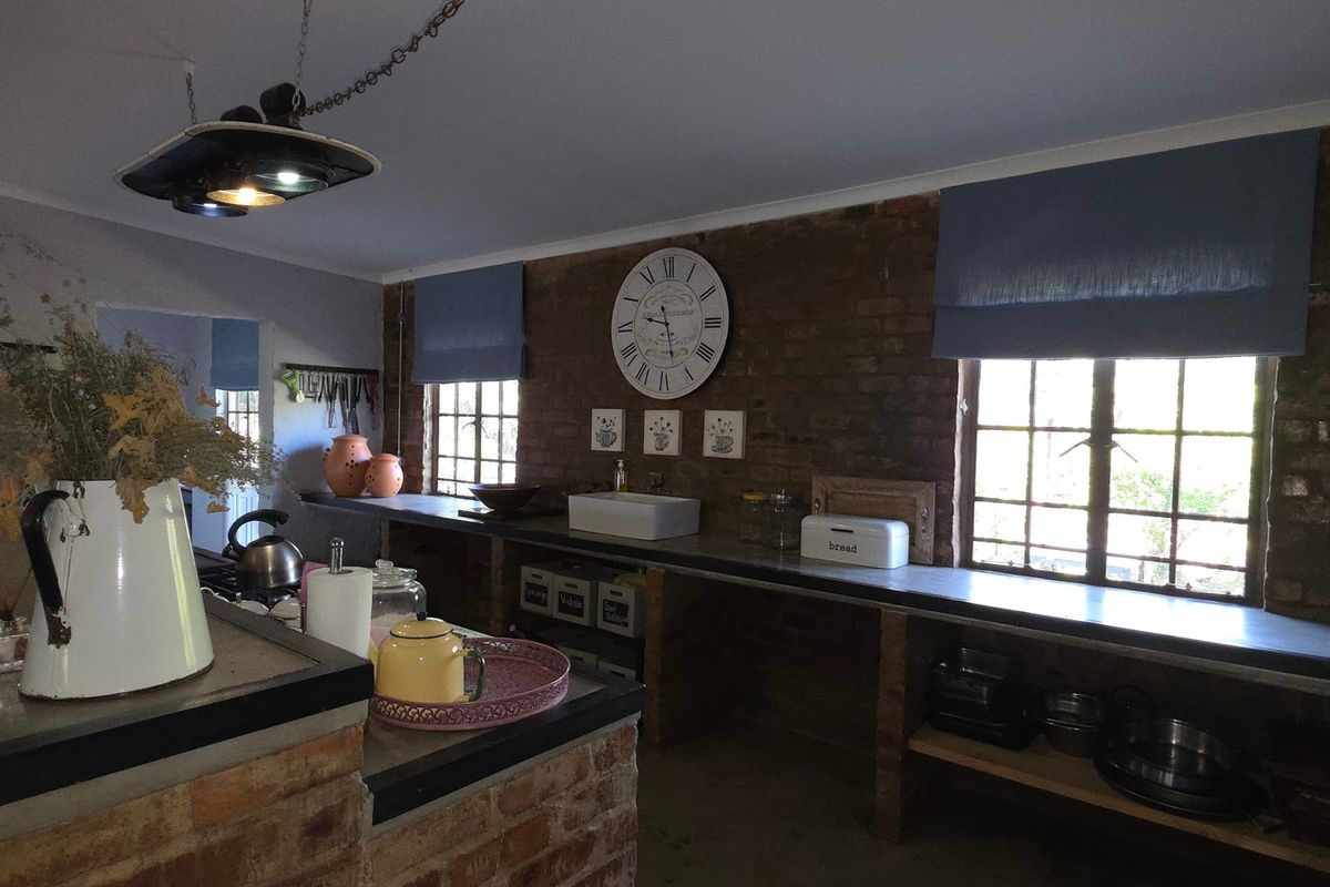 Rustic farmhouse kitchen featuring exposed brick walls, concrete countertops, a farmhouse sink, and industrial-style pendant lighting with ample natural light.
