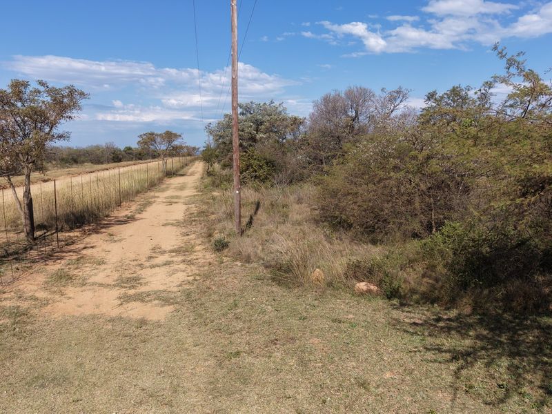 A view of a rural farm property featuring a dirt track, wire fencing, and utility infrastructure surrounded by natural vegetation.