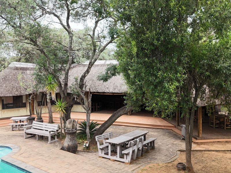 Outdoor entertainment area featuring a swimming pool, paved patio, and expansive wooden decking under a traditional thatched roof structure.