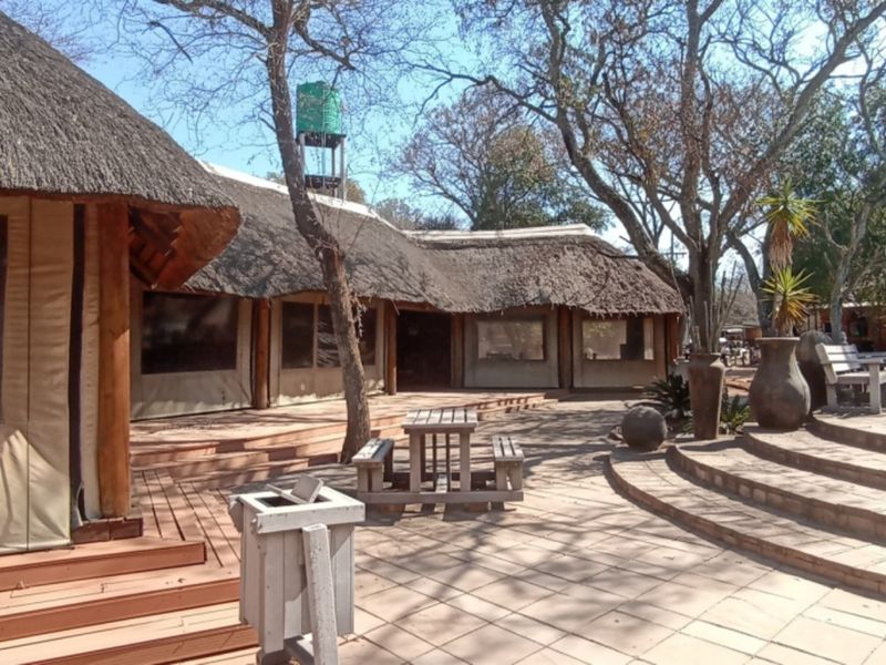 Spacious outdoor entertainment area featuring a thatched roof structure, wooden decking, and tiled patio steps leading to a pool area.