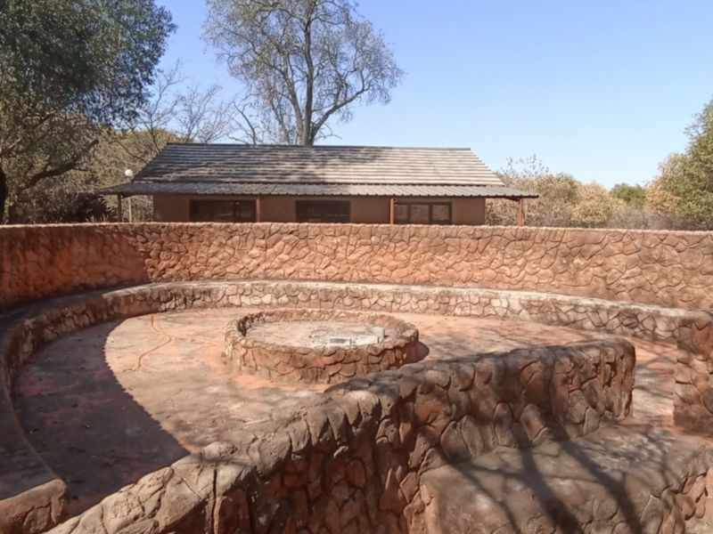 Outdoor entertainment area featuring a circular stone-clad fire pit and integrated stone seating, set within a natural bushveld environment.
