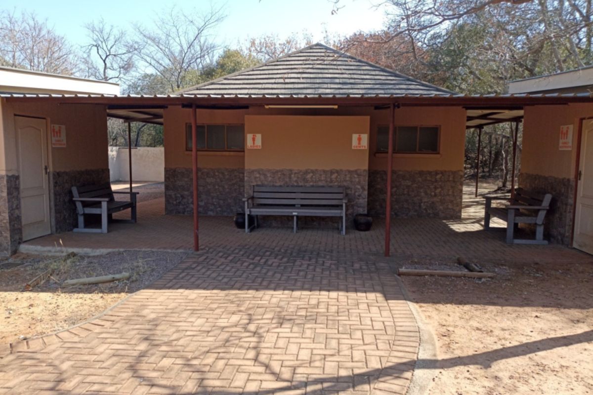 A well-maintained outdoor ablution facility featuring a covered patio area, stone-clad base, and paved access path in a natural setting.