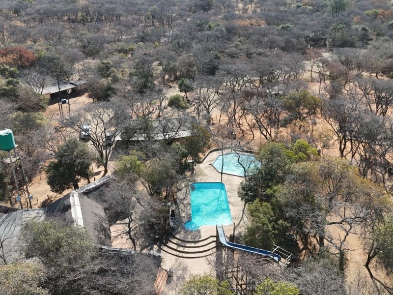 Aerial view of the small holding property featuring a swimming pool with a slide, a water tank, and multiple structures with thatched roofs.