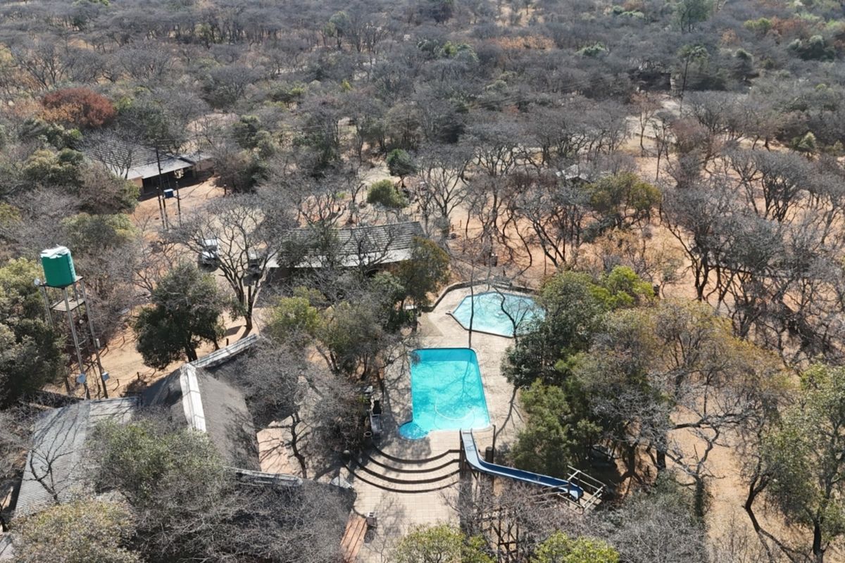 Aerial view of the small holding property featuring a swimming pool with a slide, a water tank, and multiple structures with thatched roofs.