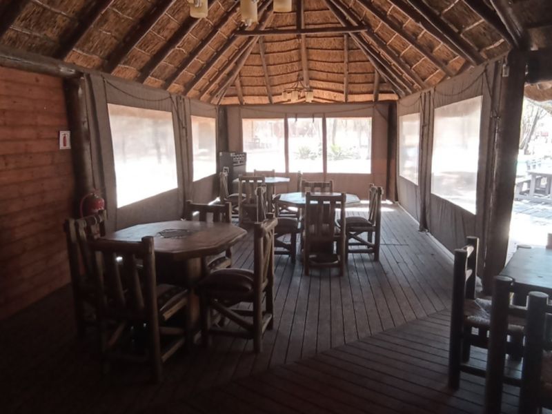 A spacious covered outdoor patio featuring a traditional thatched roof, timber decking, and roll-up canvas blinds, ideal for relaxed outdoor dining and entertainment.