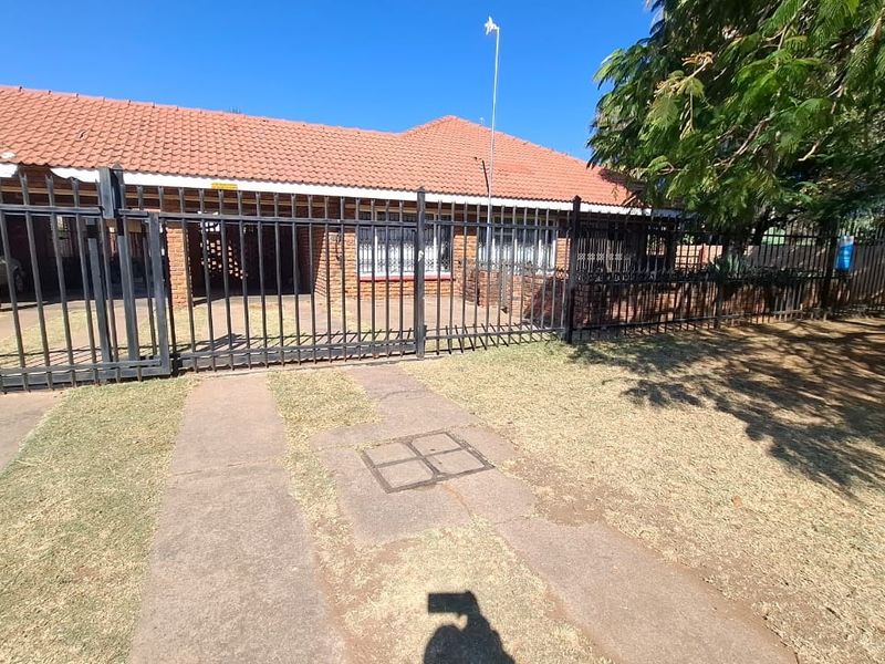 Front exterior view of a facebrick apartment building featuring a terracotta tiled roof, metal security fencing, and a paved driveway.