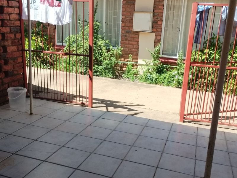 A paved outdoor patio area featuring a metal security gate, brick exterior walls, and access to the apartment interior through sliding windows.