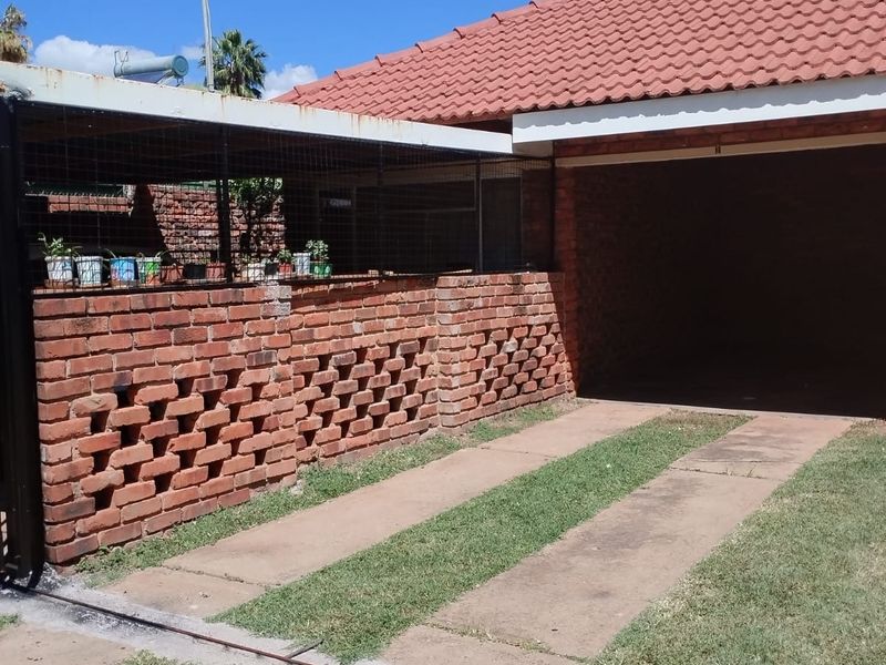 Front exterior view of the apartment featuring a brick boundary wall, tiled roof, and a concrete driveway leading to a garage.
