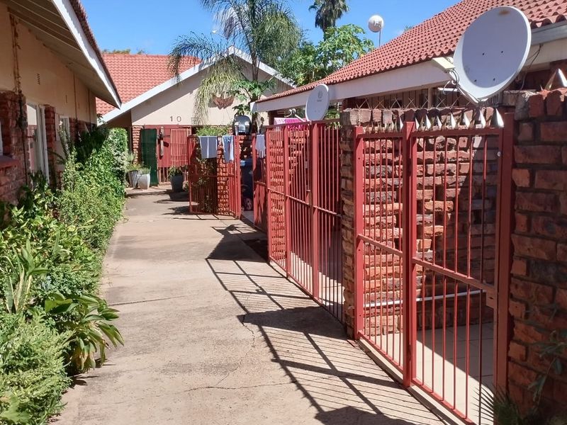 Exterior view of an apartment complex walkway featuring brick boundary walls, metal security gates, and concrete paving between residential units.