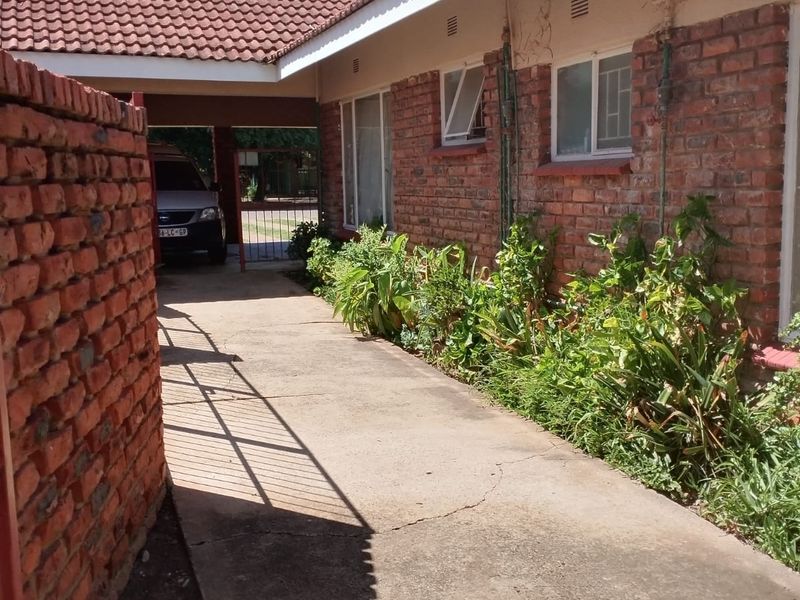 Exterior view of the apartment building featuring a brick facade, tiled roof, and a concrete driveway leading to a covered carport area.