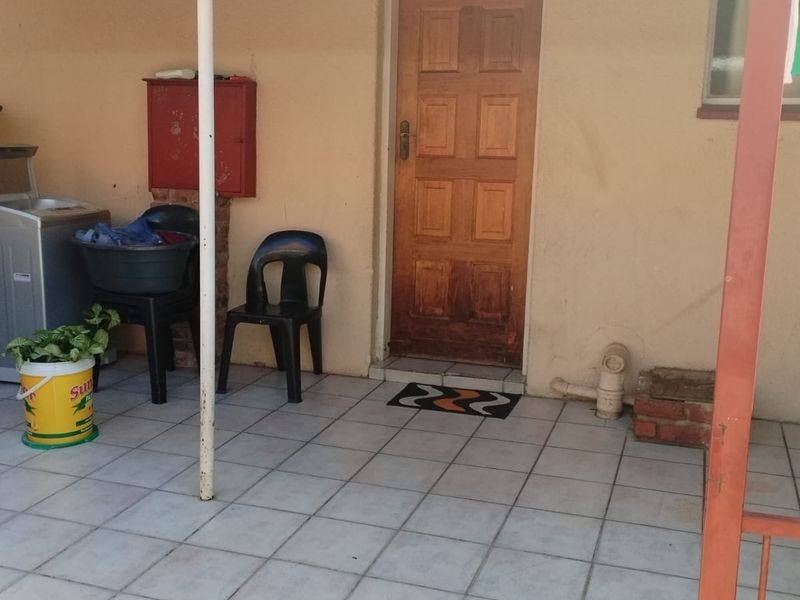 A covered patio area featuring tiled flooring and a wooden entrance door, providing a functional outdoor space for the apartment.