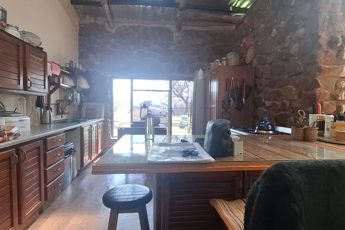 Rustic farmhouse kitchen featuring exposed stone walls, timber ceiling beams, and wooden cabinetry with a central island workspace.