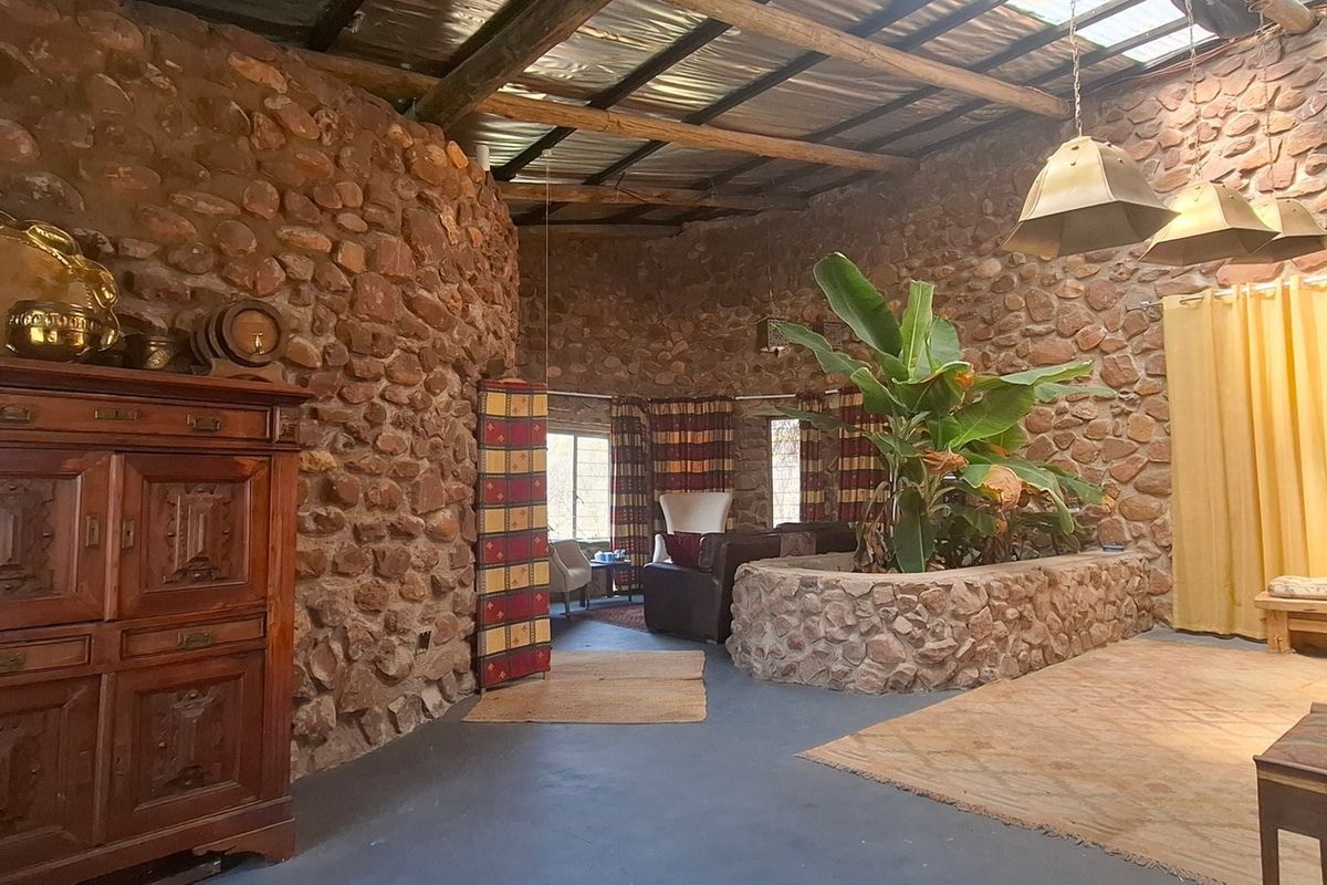 Spacious living area featuring rustic exposed stone walls, timber beam ceiling, a built-in stone planter, and natural light from a skylight.