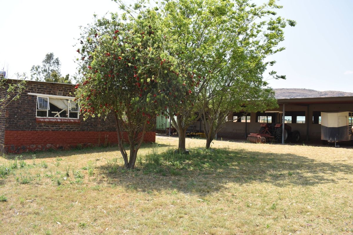 Rear view of a farm building featuring brick construction, steel window frames, and an adjacent covered storage or work area.