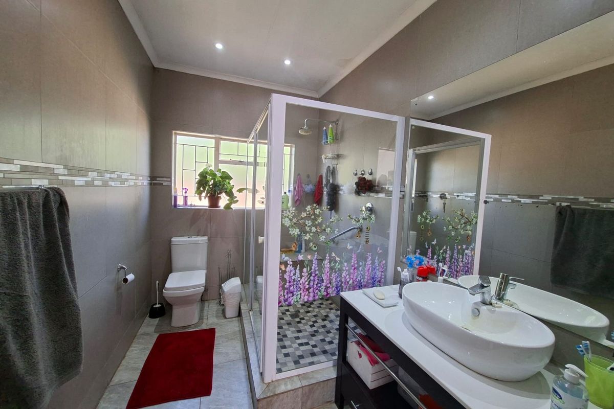 A functional bathroom featuring a glass-enclosed shower, a modern vanity basin, and neutral wall tiling with decorative accents.