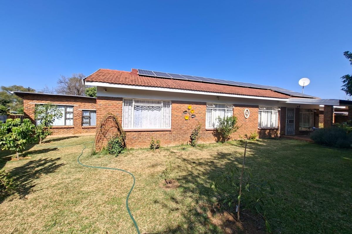 Rear view of a single-story brick house featuring a tiled roof with installed solar panels and a surrounding garden area.