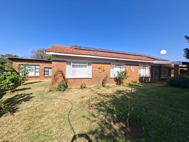 Rear view of a single-story brick house featuring a tiled roof with installed solar panels and a surrounding garden area.