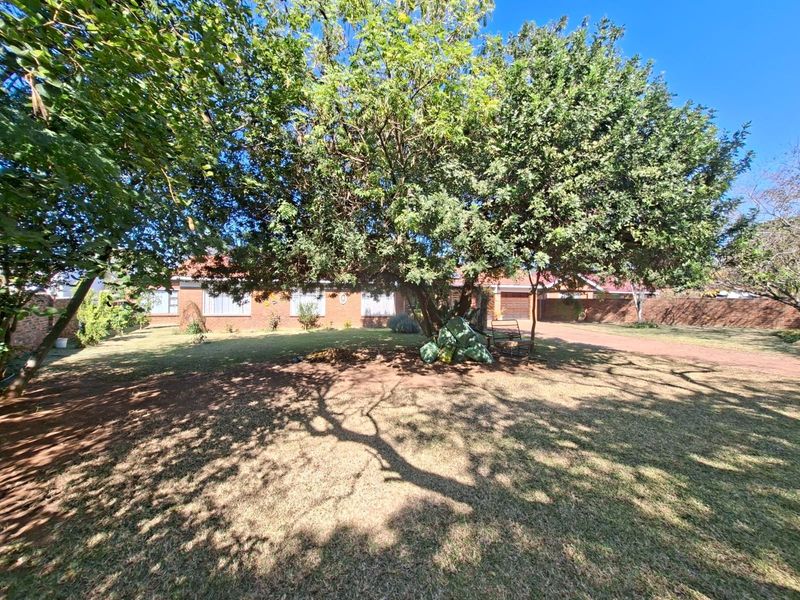 Front view of a brick house featuring a spacious lawn, mature trees, and a driveway leading to a garage.