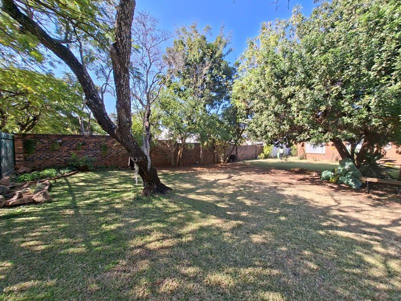 A spacious, established garden featuring mature trees, a well-maintained lawn, and a secure brick boundary wall.