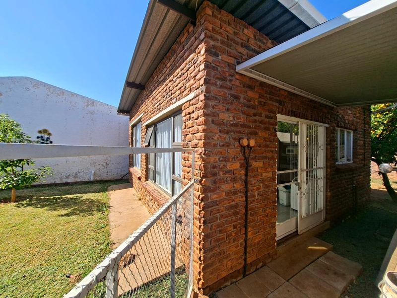 Rear view of a face brick house featuring a corrugated metal roof, security gate, and a small garden area with a paved walkway.