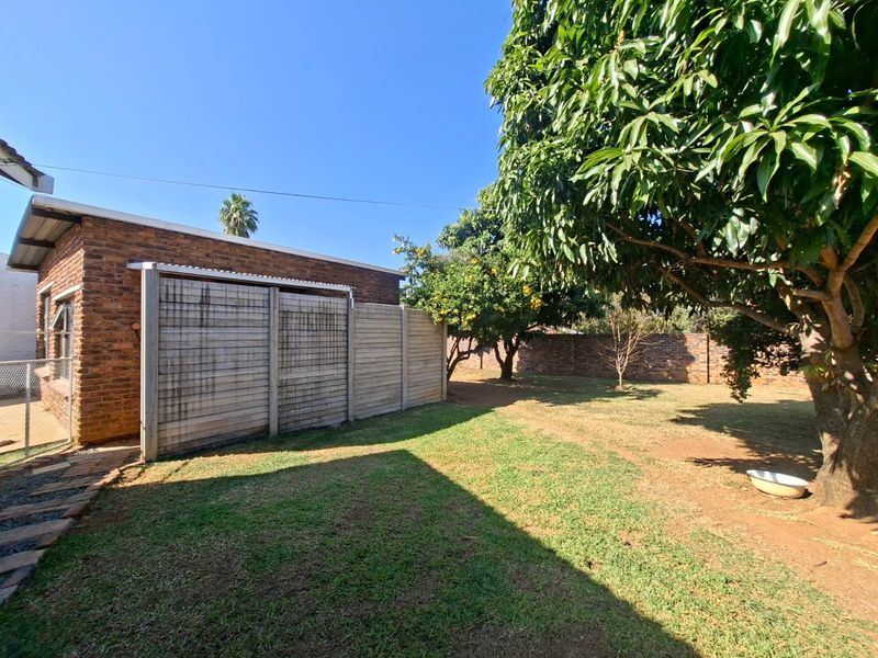 A spacious rear garden featuring a brick exterior wall, mature trees, and a precast concrete boundary wall.