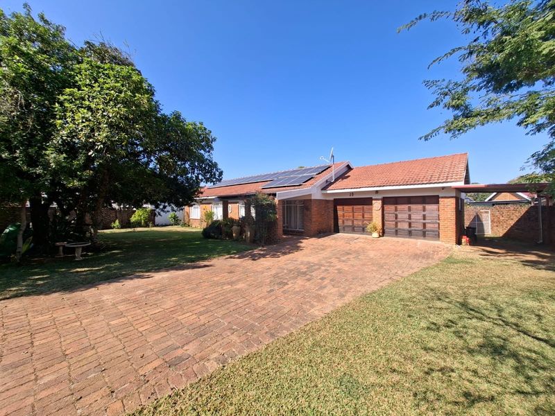 Front view of a single-story brick house featuring a paved driveway, double garage, and roof-mounted solar panels set within a landscaped garden.