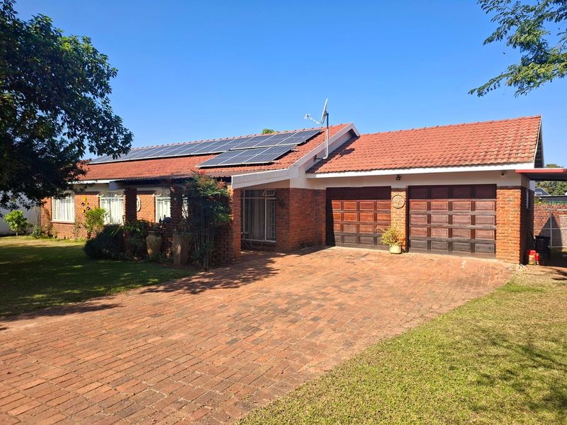 Front view of a single-story brick house featuring a double garage, paved driveway, and roof-mounted solar panels under a clear blue sky.