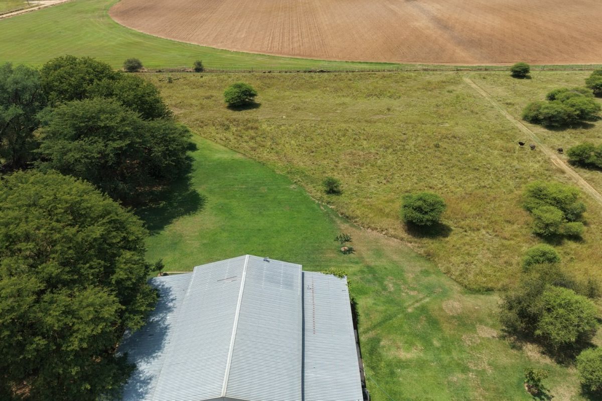 Aerial view of the small holding property featuring a large corrugated metal roof structure surrounded by expansive green lawns and open agricultural land.