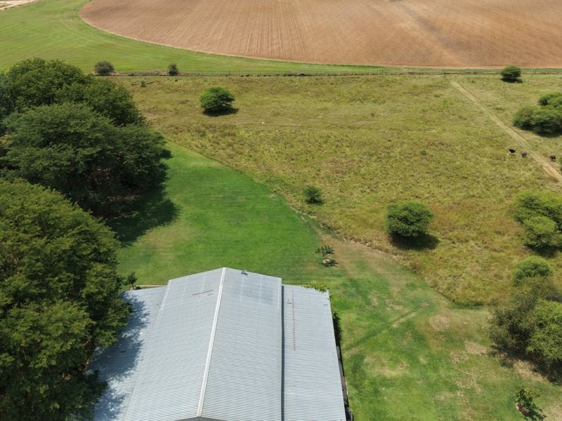 Aerial view of the small holding property featuring a large corrugated metal roof structure surrounded by expansive green lawns and open agricultural land.