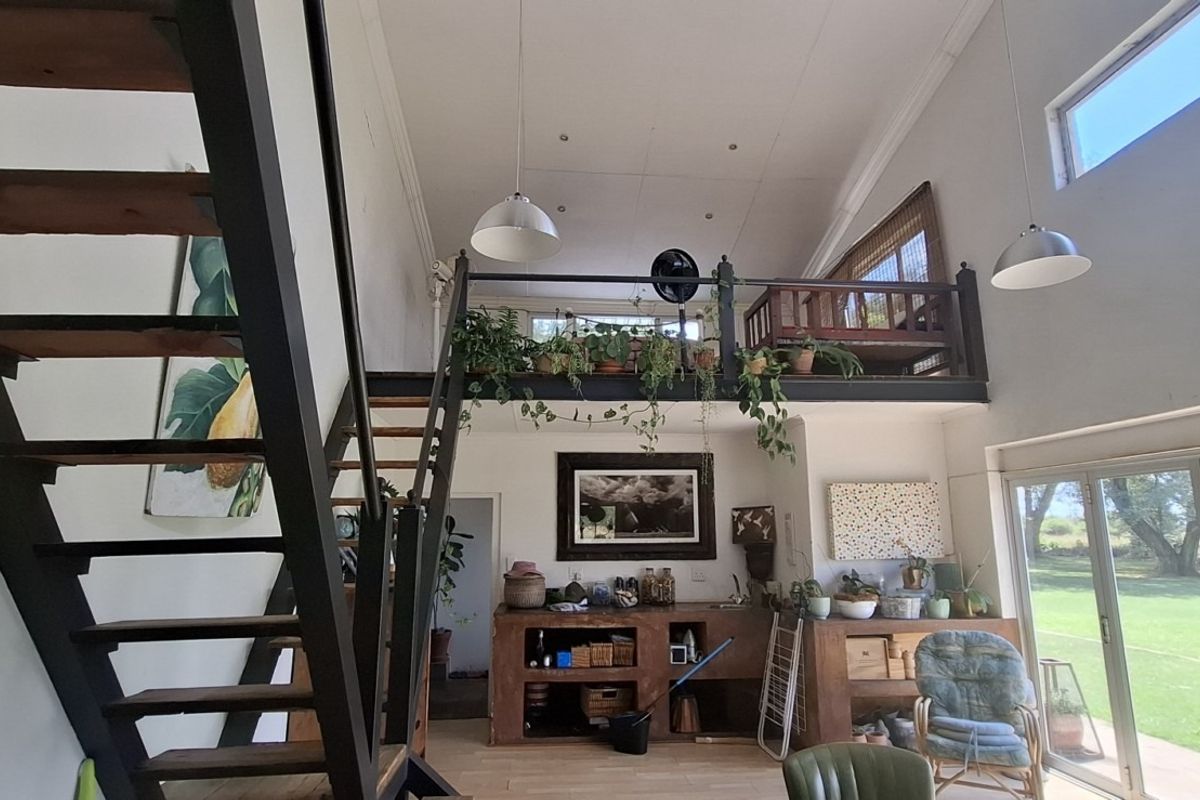 Spacious double-volume living area featuring a mezzanine level, industrial-style metal staircase, and large folding glass doors opening to the garden.