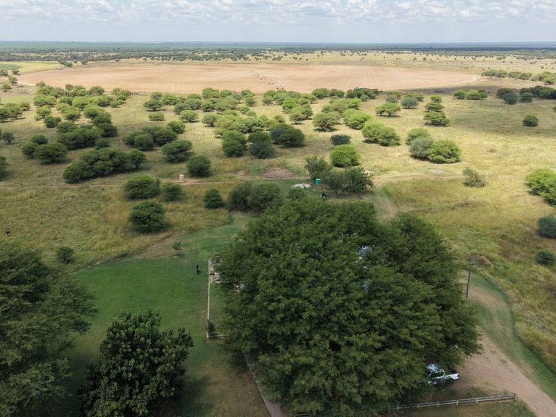 Aerial view of a large small holding property featuring expansive grazing land, mature trees, and an irrigation pivot system.