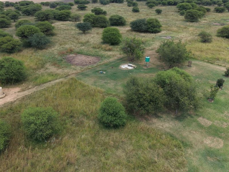Aerial view of the small holding property featuring open grazing land, indigenous trees, a water tank, and livestock watering infrastructure.