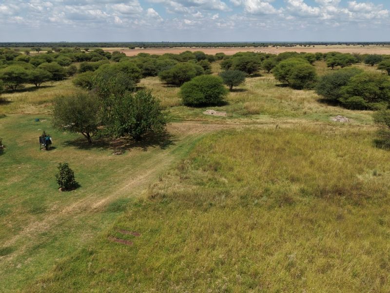An aerial view of the expansive small holding property featuring natural grassland, scattered indigenous trees, and a water storage tank.