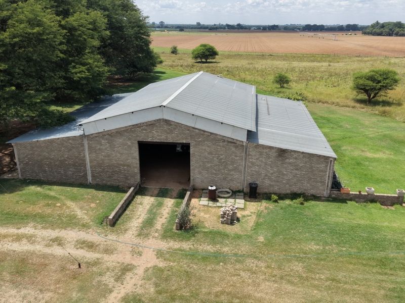 Aerial view of a large brick barn structure with a metal roof, situated on a spacious rural small holding property.
