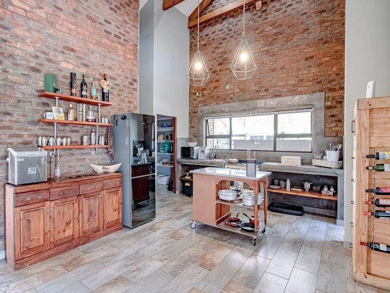 Spacious industrial-style kitchen featuring exposed brick walls, vaulted ceilings with timber beams, concrete countertops, and a convenient walk-in pantry.