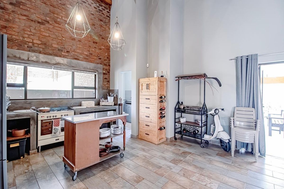 Industrial-style kitchen featuring exposed brick walls, concrete countertops, a gas stove, and tiled flooring with high ceilings and pendant lighting.