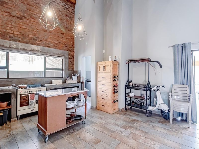 Industrial-style kitchen featuring exposed brick walls, concrete countertops, a gas stove, and tiled flooring with high ceilings and pendant lighting.