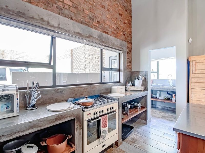 Industrial-style kitchen featuring exposed brick walls, custom concrete countertops, a gas stove, and an adjoining scullery area with tiled flooring.