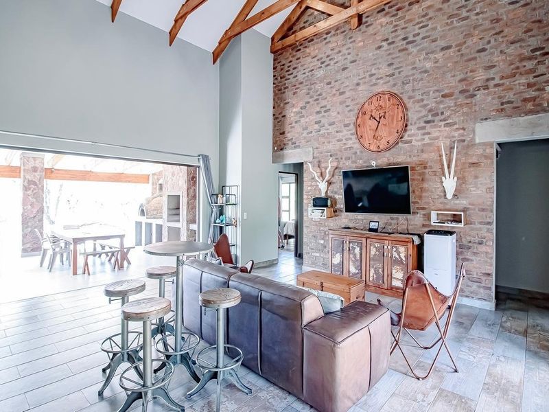 Spacious living room featuring a high vaulted ceiling with exposed timber trusses, a prominent exposed brick feature wall, and large sliding doors to the patio.