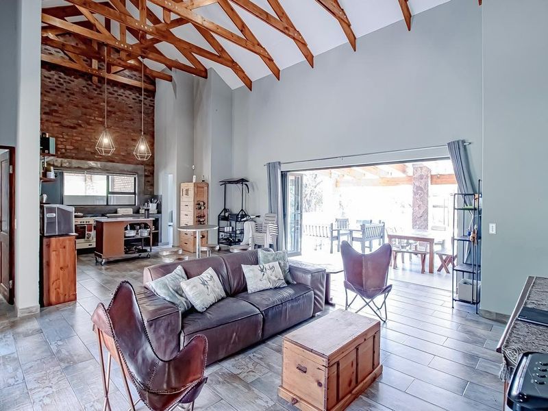 Spacious open-plan living area featuring high vaulted ceilings with exposed timber trusses, a striking brick feature wall, and seamless flow to the outdoor patio.