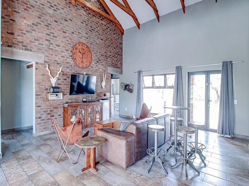 Spacious living room featuring a high vaulted ceiling with exposed timber rafters, a striking exposed brick feature wall, and large tiled flooring.