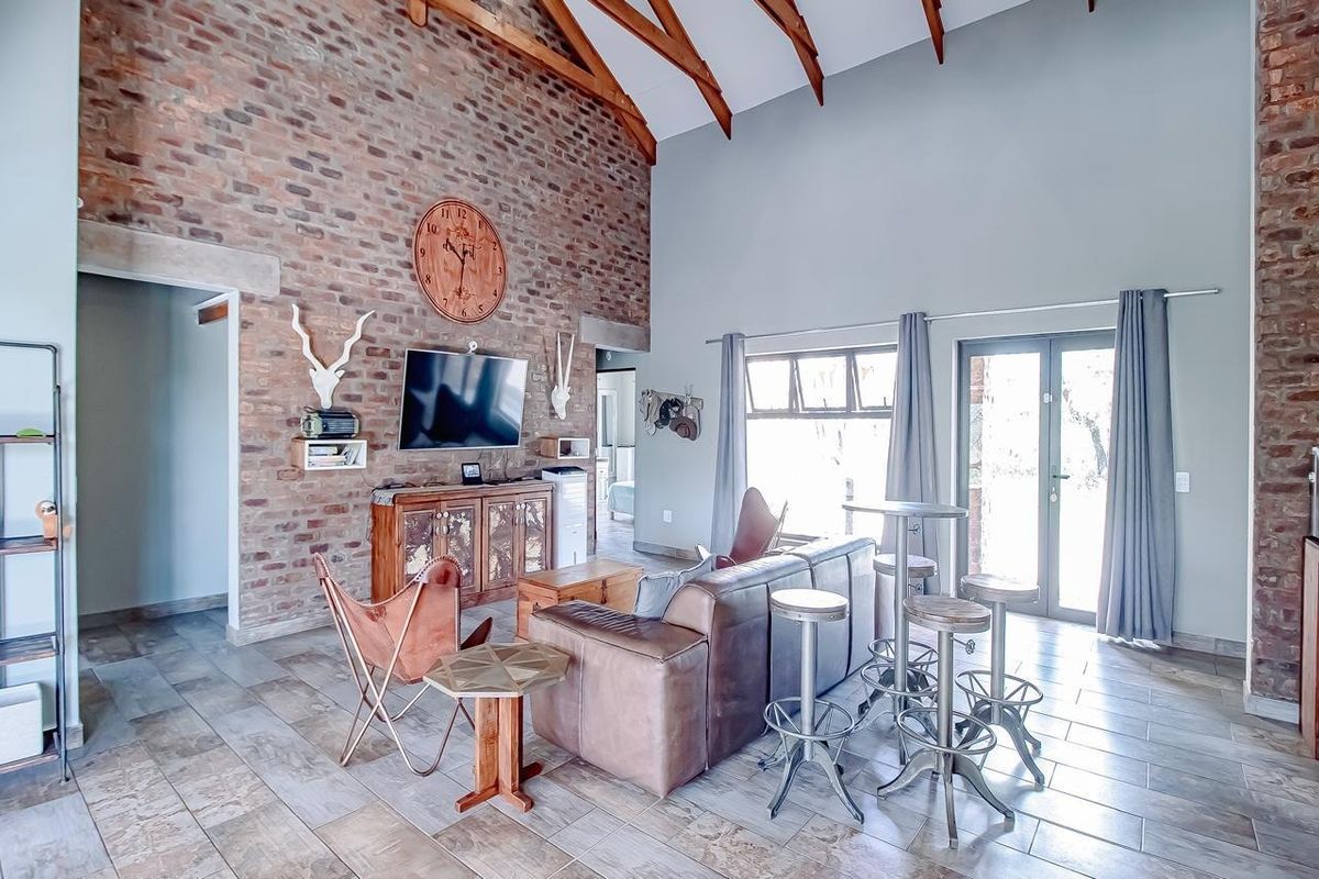 Spacious living room featuring a high vaulted ceiling with exposed timber rafters, a striking exposed brick feature wall, and large tiled flooring.
