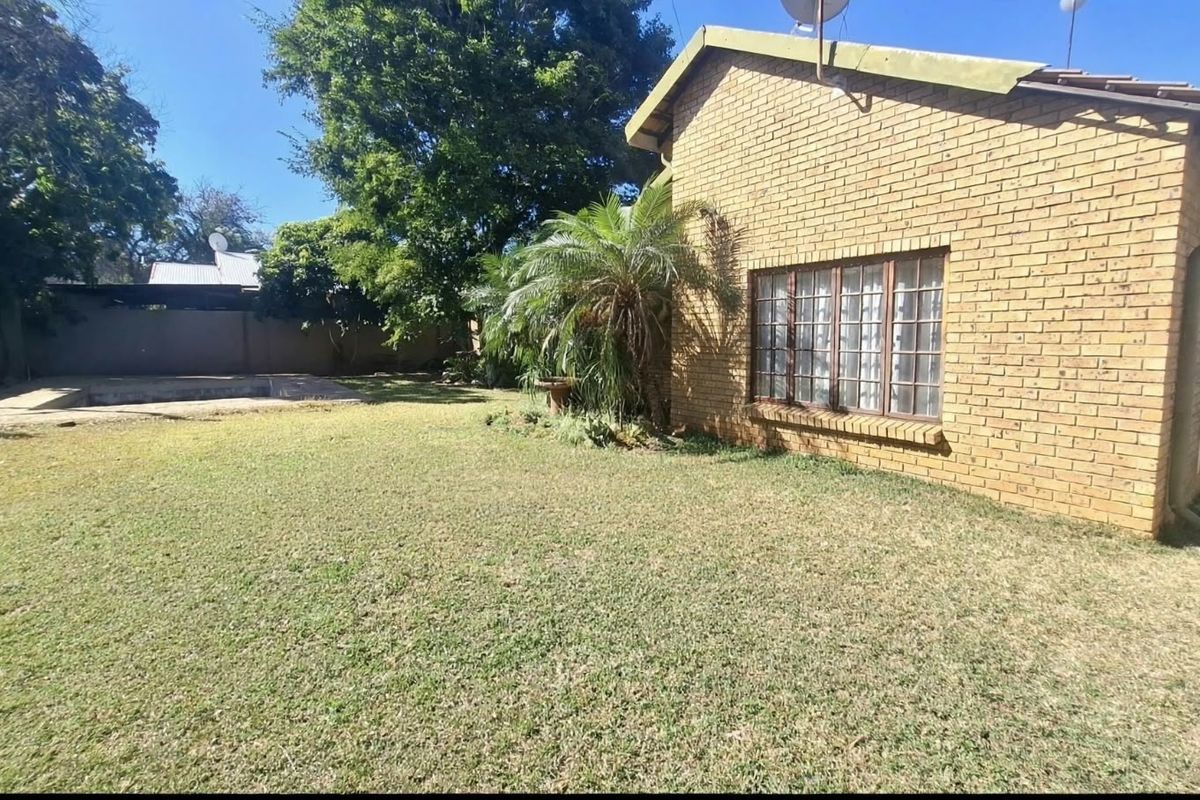 Rear view of the property featuring a face brick facade, a spacious lawn, and a swimming pool area.