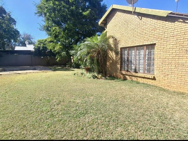 Rear view of the property featuring a face brick facade, a spacious lawn, and a swimming pool area.