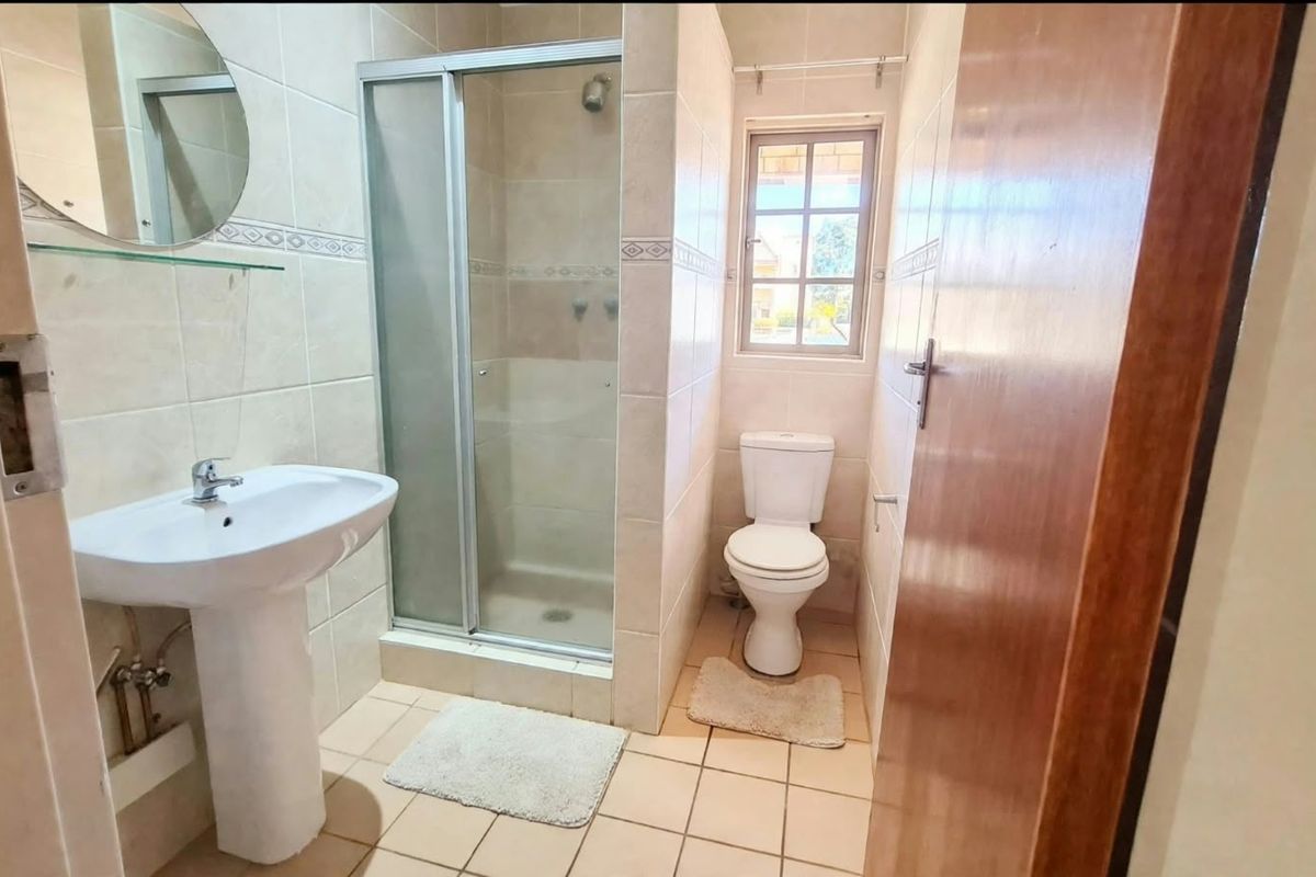 A functional bathroom featuring a pedestal basin, a glass-enclosed shower, and a toilet, finished with neutral wall and floor tiles.