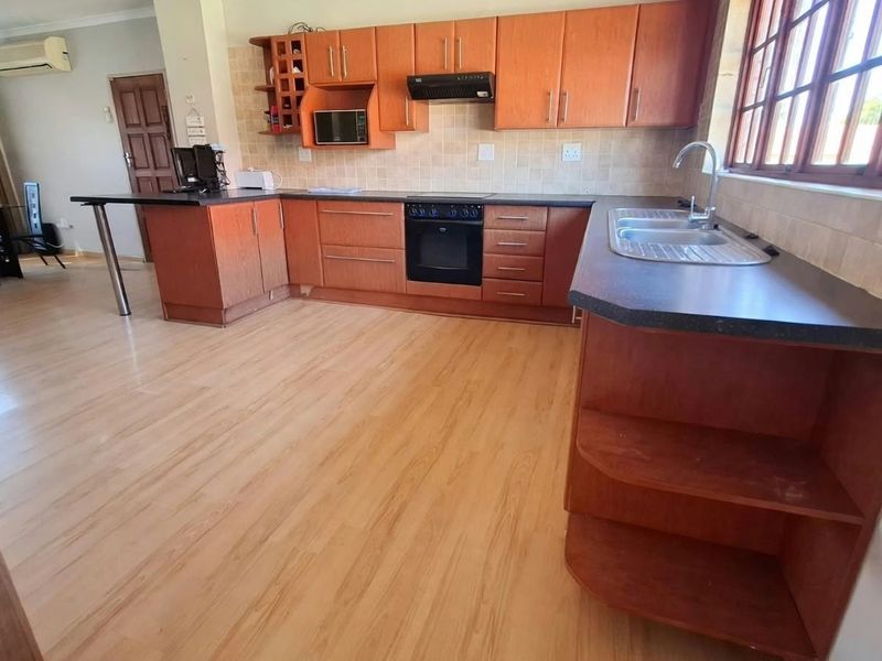 Open-plan kitchen featuring wooden cabinetry, laminate countertops, built-in oven, and extractor fan, seamlessly flowing into the adjacent living and dining area.